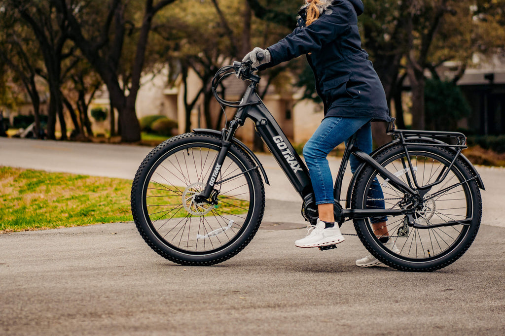 A shot of a woman standing with the GOTRAX MX1 Mid-Drive eBike with an 82 mile range and pneumatic tires.