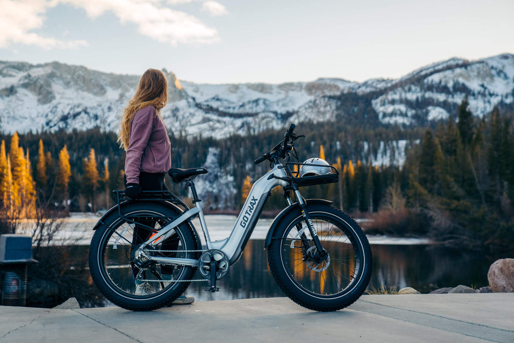 A woman standing next to the GOTRAX Tundra Fat Tire eBike with a torque sensor and 750 watt motor looking out on to a mountain lake.
